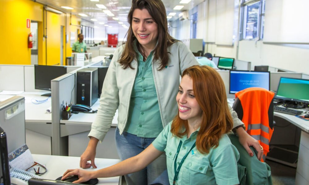 Vale oferece 112 vagas para cursos técnicos no ES com bolsa de R$ 2.120 Duas funcionárias da Vale trabalhando em um escritório, interagindo diante de um computador.