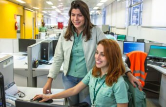 Duas funcionárias da Vale trabalhando em um escritório, interagindo diante de um computador.