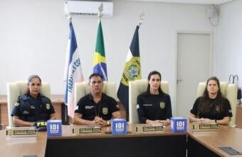 Quatro autoridades de segurança, incluindo uma agente da PRF e três membros da Polícia Civil, sentados à mesa durante a coletiva de imprensa que detalhou a prisão do suspeito de tentativa de feminicídio Serra ES. À frente deles, destacam-se as bandeiras oficiais e as placas do 181 Disque Denúncia.