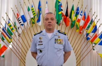 Coronel Douglas Caus em uniforme oficial diante de bandeiras no ES, ex-titular do comando da Polícia Militar do ES.