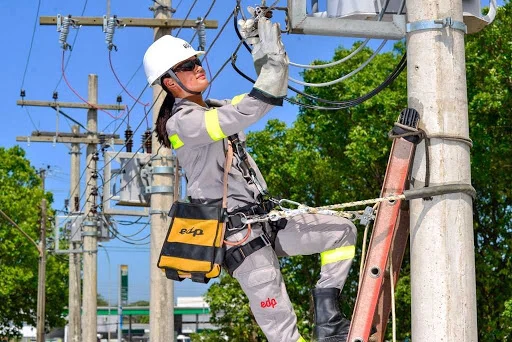 EDP abre curso gratuito de eletricista na Serra com bolsa de R$ 900 Fotografia de uma trainee em treinamento prático no Senai Serra conectando cabos elétricos, com sobreposição de texto em português: "Curso Gratuito de Eletricista. Bolsa de Estudo: R$ 900. Inscrições Abertas em Serra ES". Logotipos da EDP e Senai Serra visíveis.
