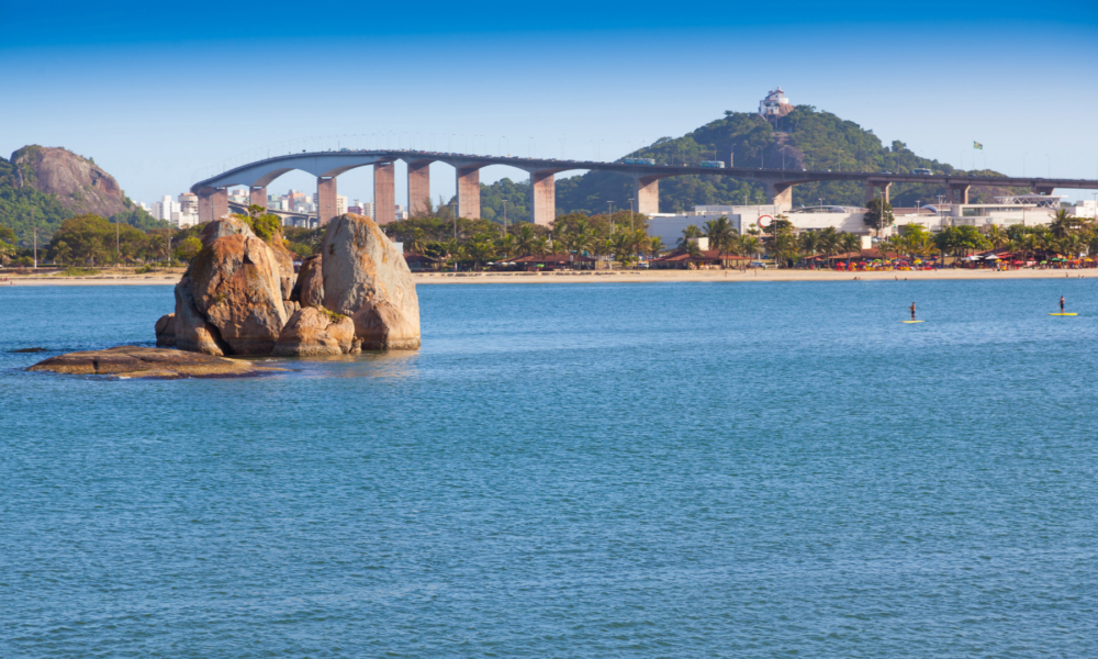 Vista panorâmica dos destinos turísticos do Espírito Santo com a Terceira Ponte de Vitória, formações rochosas no mar e o Convento da Penha ao fundo