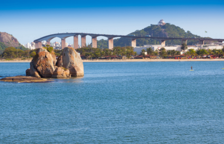Vista panorâmica dos destinos turísticos do Espírito Santo com a Terceira Ponte de Vitória, formações rochosas no mar e o Convento da Penha ao fundo