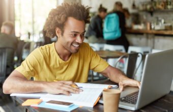 Estudante com cabelo cacheado sorrindo enquanto anota em caderno ao aplicar dicas de estudo Enem 2026.