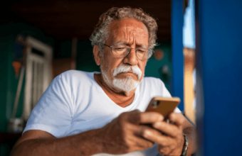 Idoso preocupado olhando o celular ao verificar descontos indevidos de empréstimo consignado no Espírito Santo.