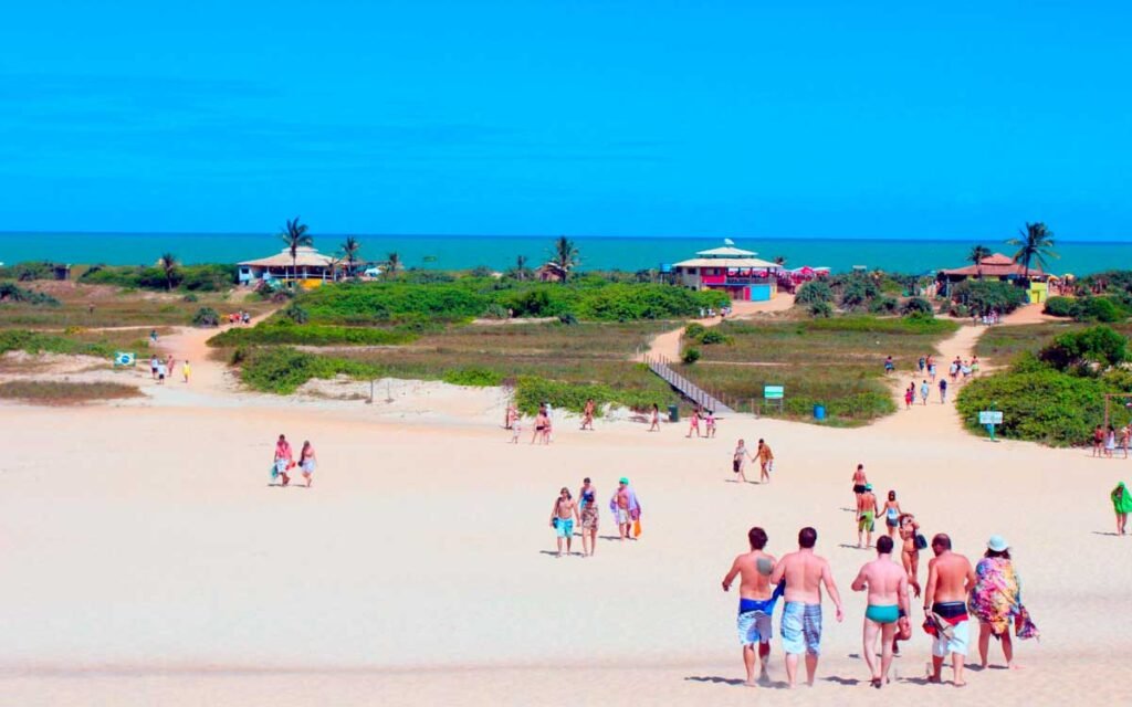 Praia de Itaúnas em Conceição da Barra, Espírito Santo, com areia branca, vegetação de restinga e banhistas — um dos destinos turísticos mais procurados do ES