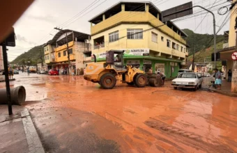 Máquina da prefeitura retira lama de rua alagada no centro após chuva forte em Muniz Freire e Pedra Azul.