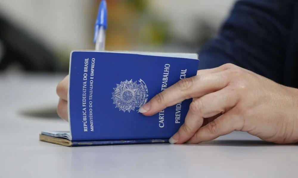 Mãos preenchendo Carteira de Trabalho azul (CTPS) física onde estão abertas mais de 4 mil vagas de emprego no ES.