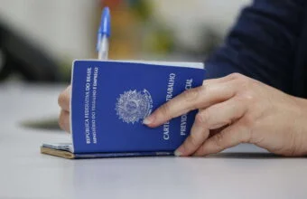 Mãos preenchendo Carteira de Trabalho azul (CTPS) física onde estão abertas mais de 4 mil vagas de emprego no ES.