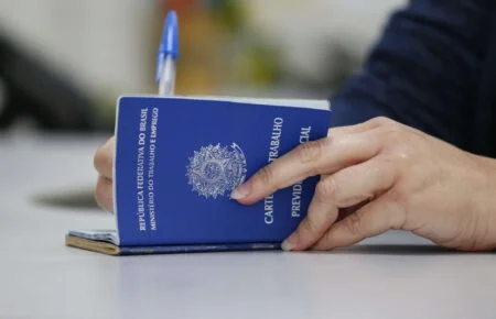 Mãos preenchendo Carteira de Trabalho azul (CTPS) física onde estão abertas mais de 4 mil vagas de emprego no ES.