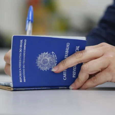 Mãos preenchendo Carteira de Trabalho azul (CTPS) física onde estão abertas mais de 4 mil vagas de emprego no ES.