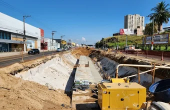 Canteiro de obras em horário de pico na Grande Vitória com gerador CAT e escavação profunda ocupando pistas centrais.