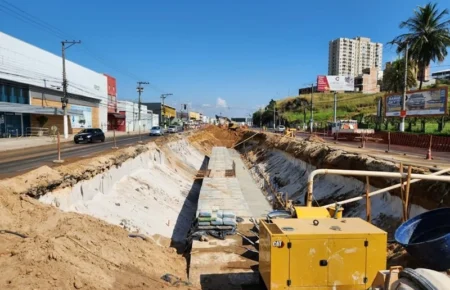 Canteiro de obras em horário de pico na Grande Vitória com gerador CAT e escavação profunda ocupando pistas centrais.