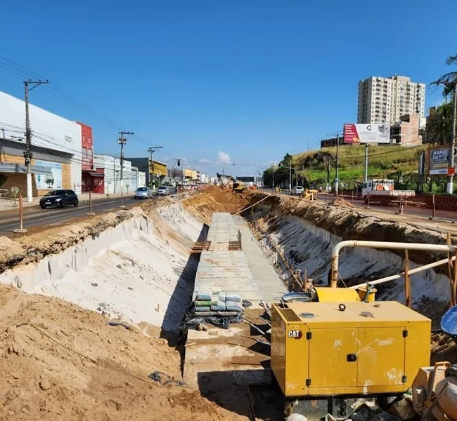 Canteiro de obras em horário de pico na Grande Vitória com gerador CAT e escavação profunda ocupando pistas centrais.
