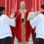 Papa Leão 14 com vestes vermelhas e mãos erguidas em oração durante missa de Papa Leão 14 Domingo de Ramos 2026 no Vaticano.