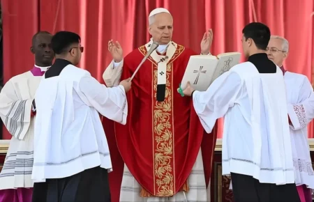 Papa Leão 14 com vestes vermelhas e mãos erguidas em oração durante missa de Papa Leão 14 Domingo de Ramos 2026 no Vaticano.