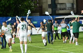 Jogadores de futebol vestindo uniformes brancos com detalhes em verde comemoram intensamente no gramado à noite, girando camisas no ar e celebrando a classificação do Porto Vitória para a final do Capixabão.