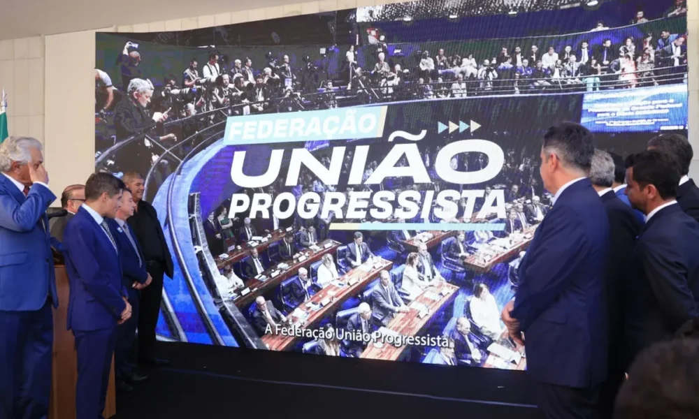 Políticos assistem ao anúncio da federação União Progressista em grande telão na Câmara dos Deputados.