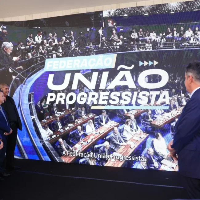 Políticos assistem ao anúncio da federação União Progressista em grande telão na Câmara dos Deputados.
