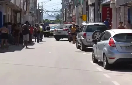 Rua isolada com fita amarela pela polícia após caso de violencia Terra Vermelha Vila Velha, com viatura estacionada no centro da via e diversos moradores observando a cena do crime nas calçadas.